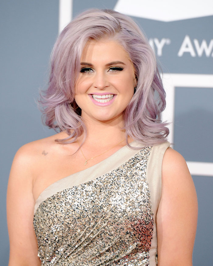 Kelly Osbourne with lavender hair and sparkling one-shoulder dress drawing Hollywood attention at a public event.