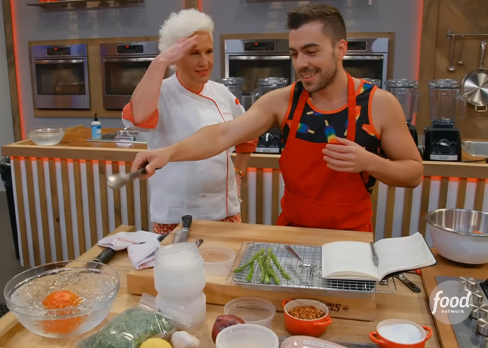 Anne Burrell cooking in a kitchen, smiling and interacting with a young man while preparing food ingredients. Anne Burrell cooking in a kitchen, smiling and interacting with a young man while preparing food ingredients.