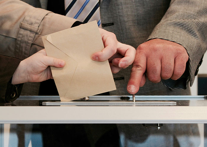 Hands placing a ballot into a transparent voting box, illustrating one of the things countries have that just make sense.