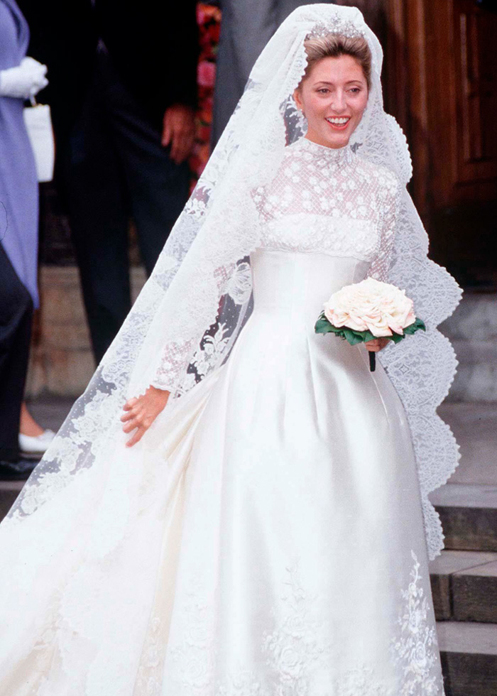 Bride in a royal wedding dress with lace veil and long sleeves, holding a bouquet, sparking buzz in wedding fashion.