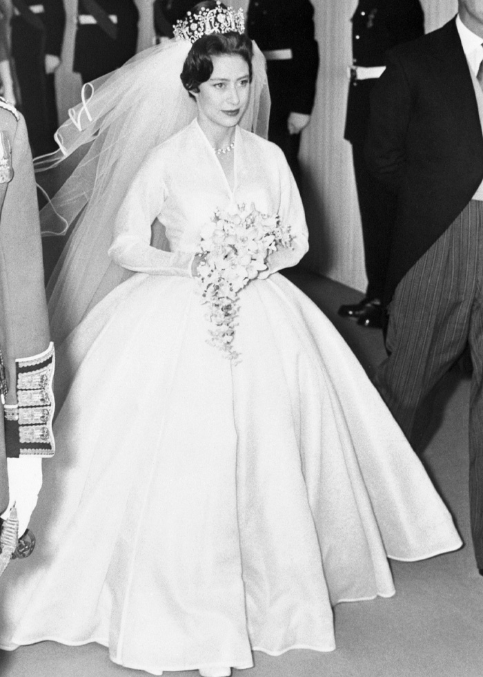 Black and white photo of a royal bride in a classic wedding dress and tiara holding a bouquet at a formal wedding event.