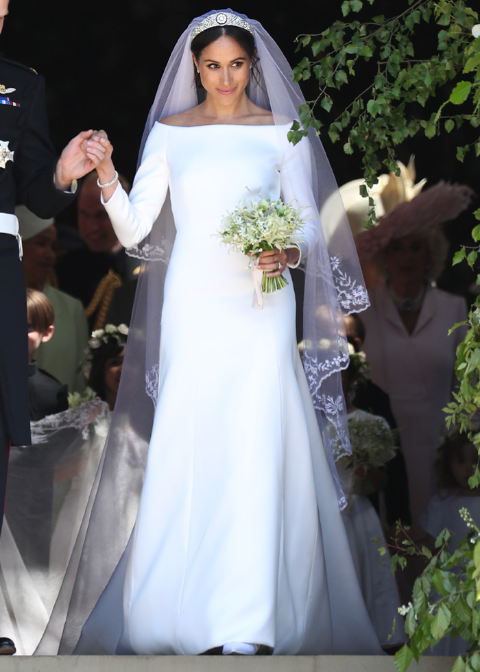 Bride wearing a classic royal wedding dress with long veil and tiara, holding a bouquet of flowers during a wedding ceremony.