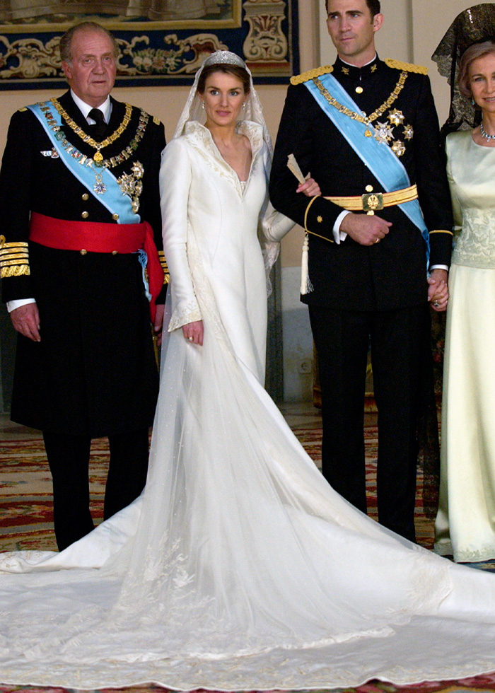 Bride wearing a royal wedding dress with long train and tiara, standing with formally dressed men in military attire.
