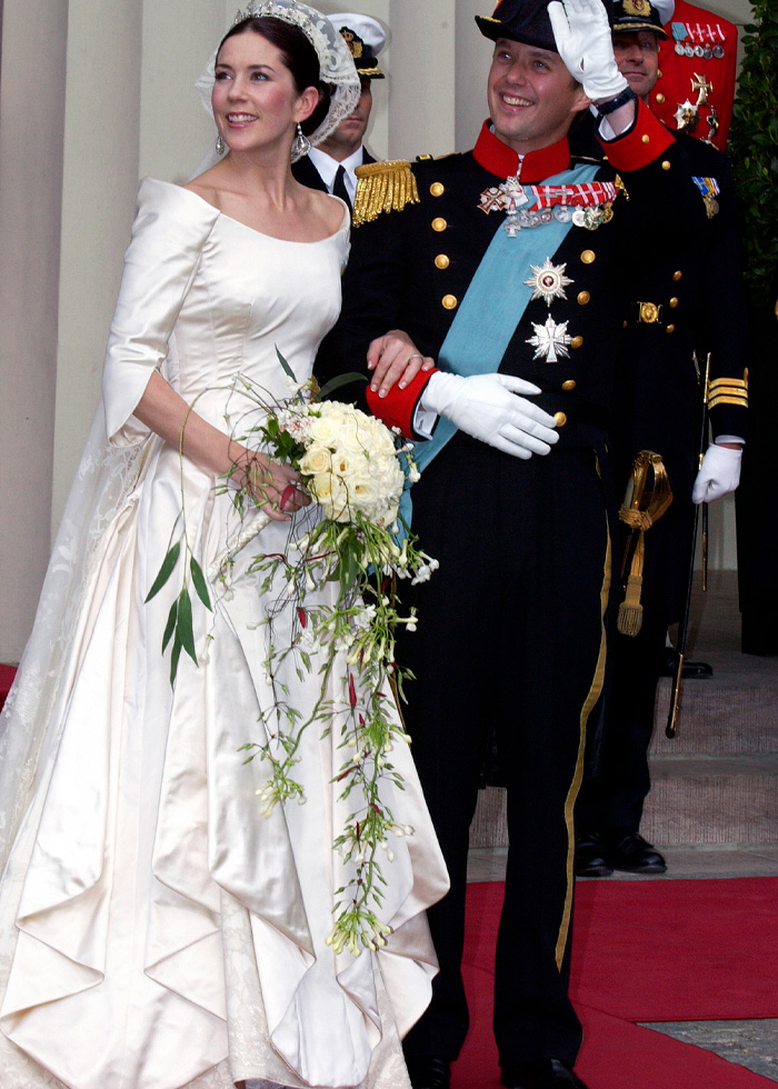 Bride in a traditional royal wedding dress holding a cascading bouquet, standing beside a groom in formal military attire.
