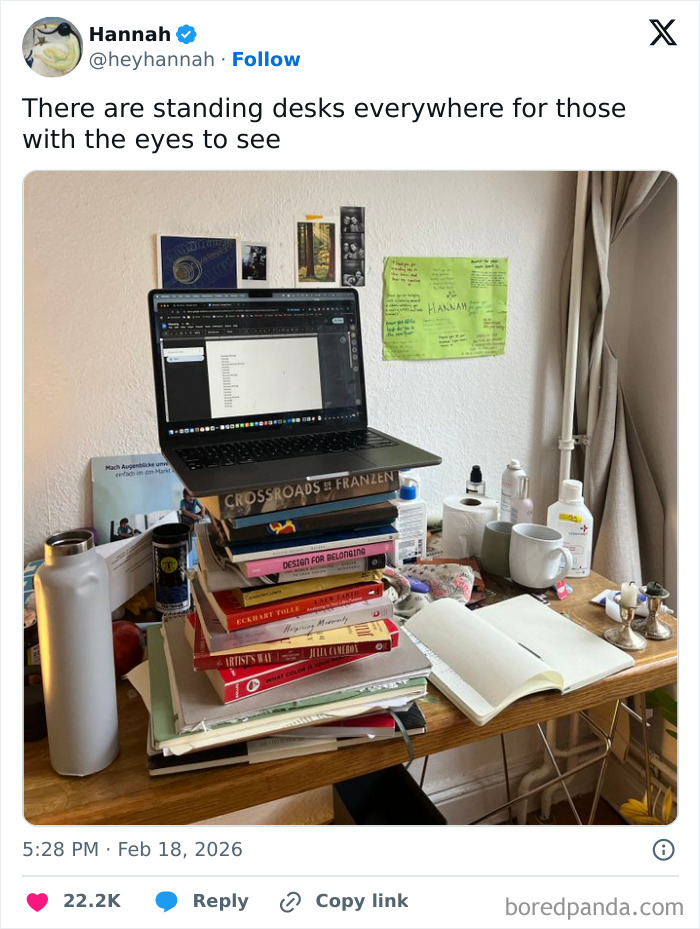 Laptop on a makeshift standing desk made of stacked books in a cluttered room, showcasing chaotic and hilarious X posts.