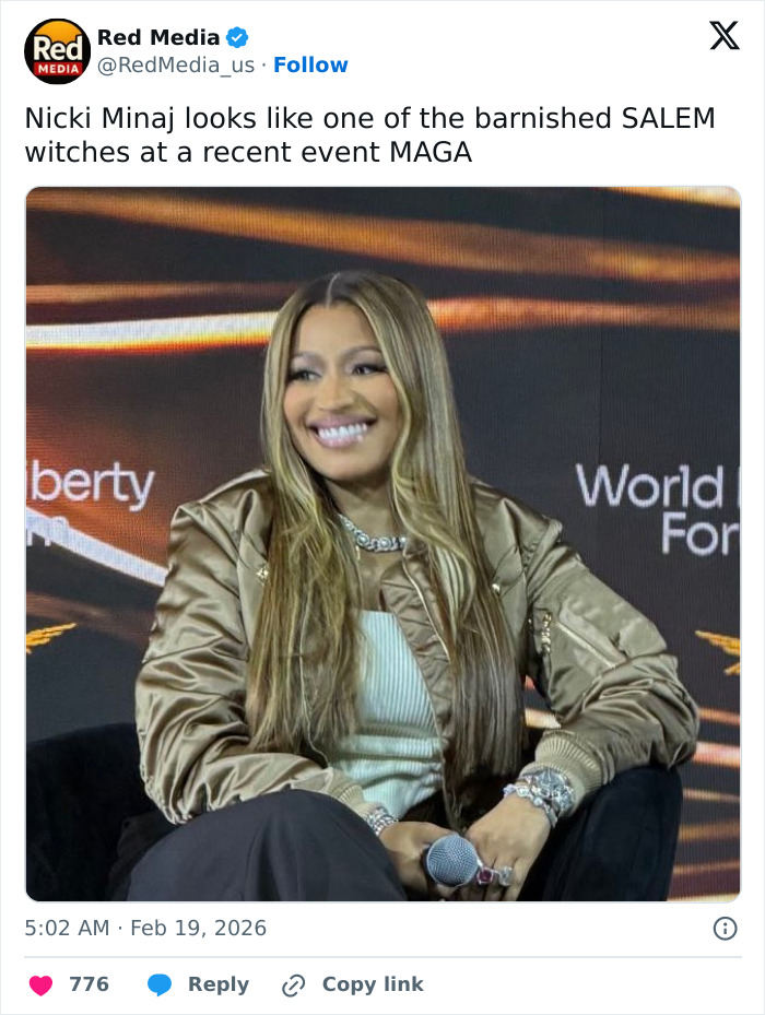 Nicki Minaj with long blonde hair and gold jacket smiling during a panel discussion at an event.
