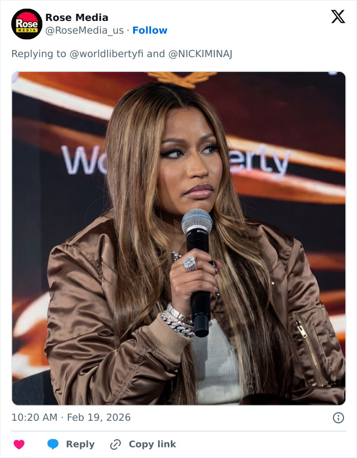 Nicki Minaj with long highlighted hair and brown jacket speaking into microphone at an event panel discussion