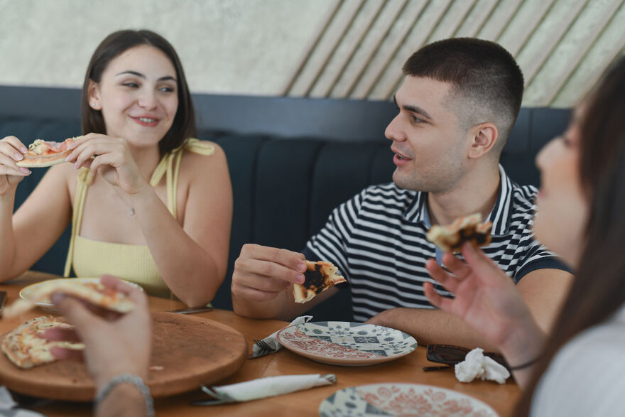 Group of young adults eating pizza together, showing common pet peeves that divide a room during mealtime conversations.