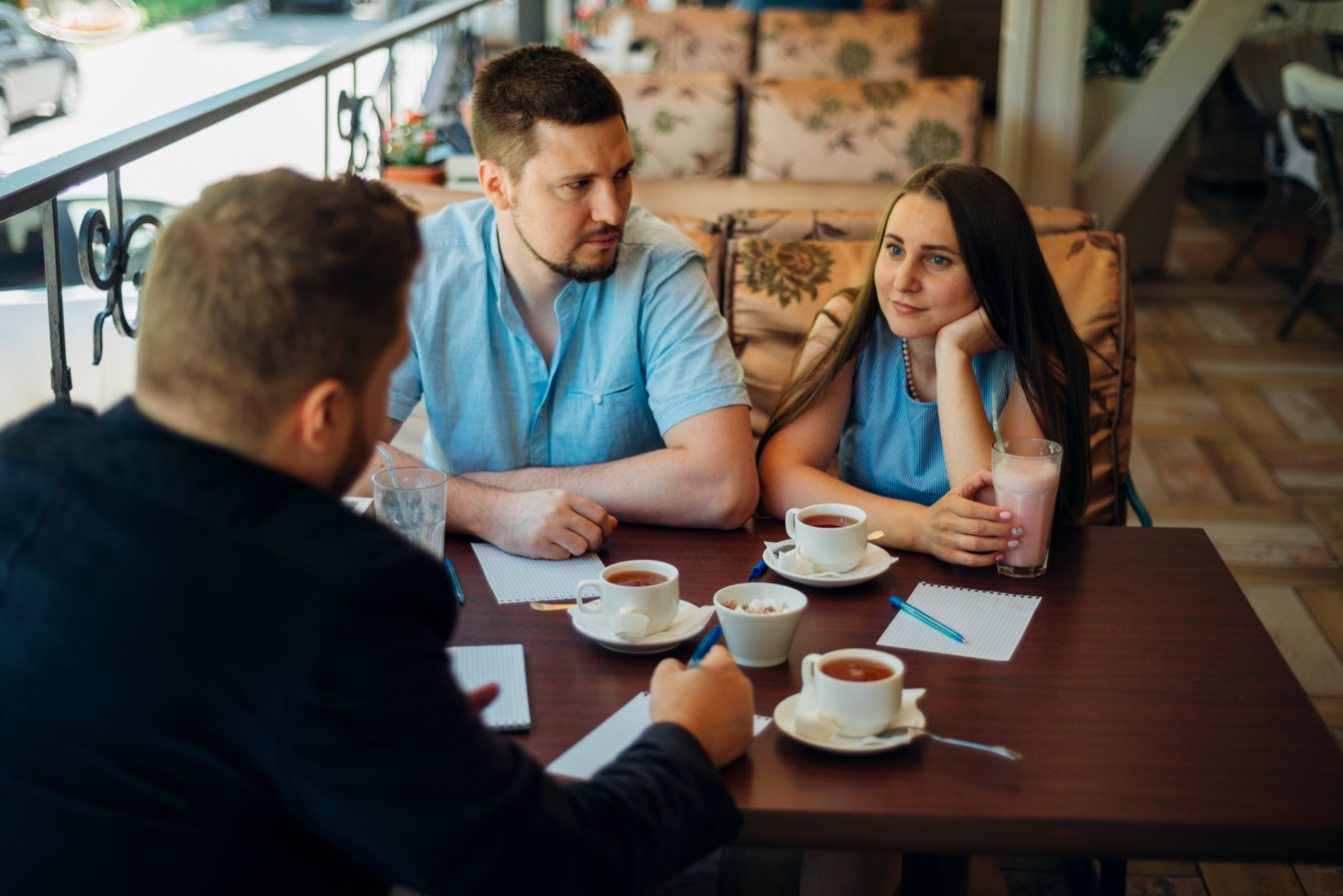 Nervous guy and his bestie chaperone first date at cafe with drinks and notes, woman looks annoyed at the situation.