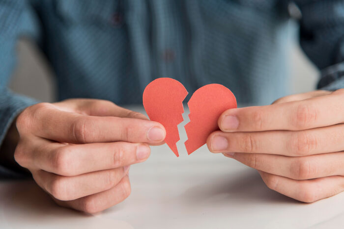 Hands holding a broken red paper heart symbolizing brutal wake-up calls in nasty situations and urgent self-removal.