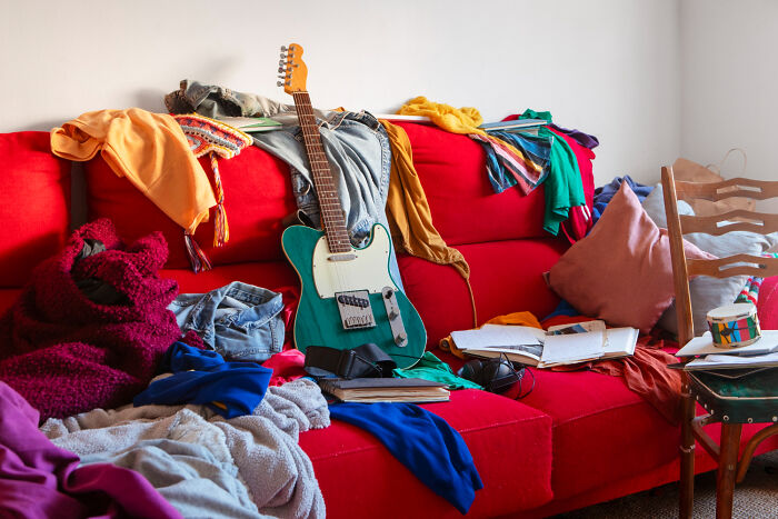 Messy red couch cluttered with clothes, books, and an electric guitar symbolizing a brutal wake-up call to leave a nasty situation.