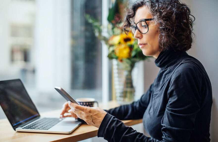 Woman with glasses working on laptop and phone at cafe, illustrating common pet peeves that divide a room.