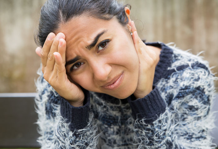 Woman looking stunned and stressed while holding her head, reacting to unexpected intrusion by roommate&rsquo;s parents.