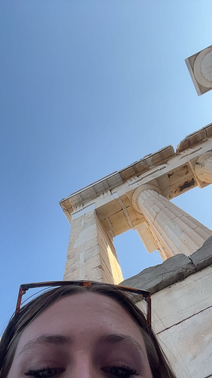 Mom taking a funny chaotic energy selfie with ancient stone columns and clear blue sky in the background.