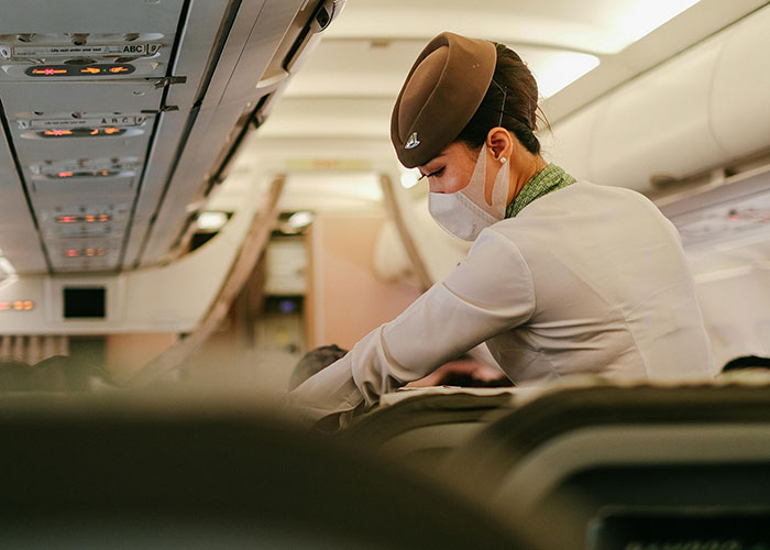 Flight attendant wearing a mask serving passengers on a plane during a travel encounter with a kind stranger.