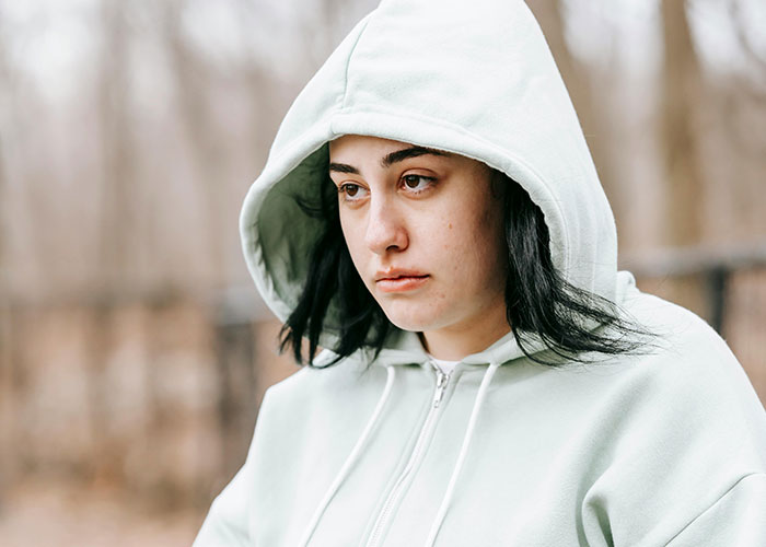 Young woman in a white hoodie looking sad outdoors, representing dad choosing new family over daughter situation.