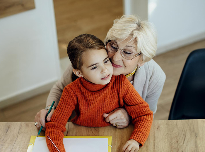 Sassy teen girl with blonde hair sitting with her grandmother at a table, sharing a moment indoors.