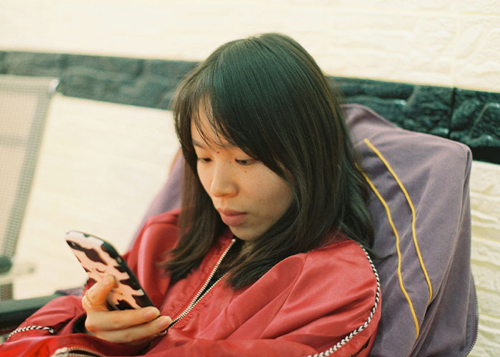 Young woman in a red jacket looking at her phone, illustrating concerns related to North Korea public executions and Squid Game.
