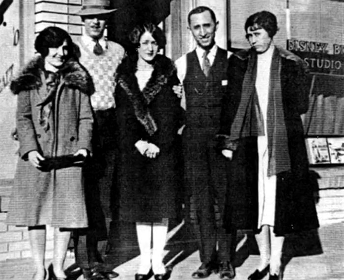 Group of five people dressed in 1920s clothing standing outside Disney Bros Studio in rare historical photo.