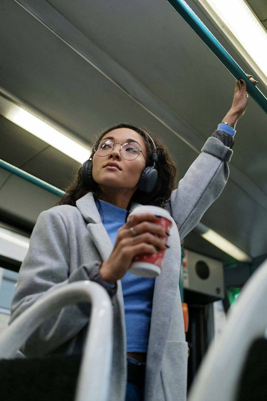 Woman wearing headphones and glasses on public transport holding a drink, illustrating common pet peeves in shared spaces.