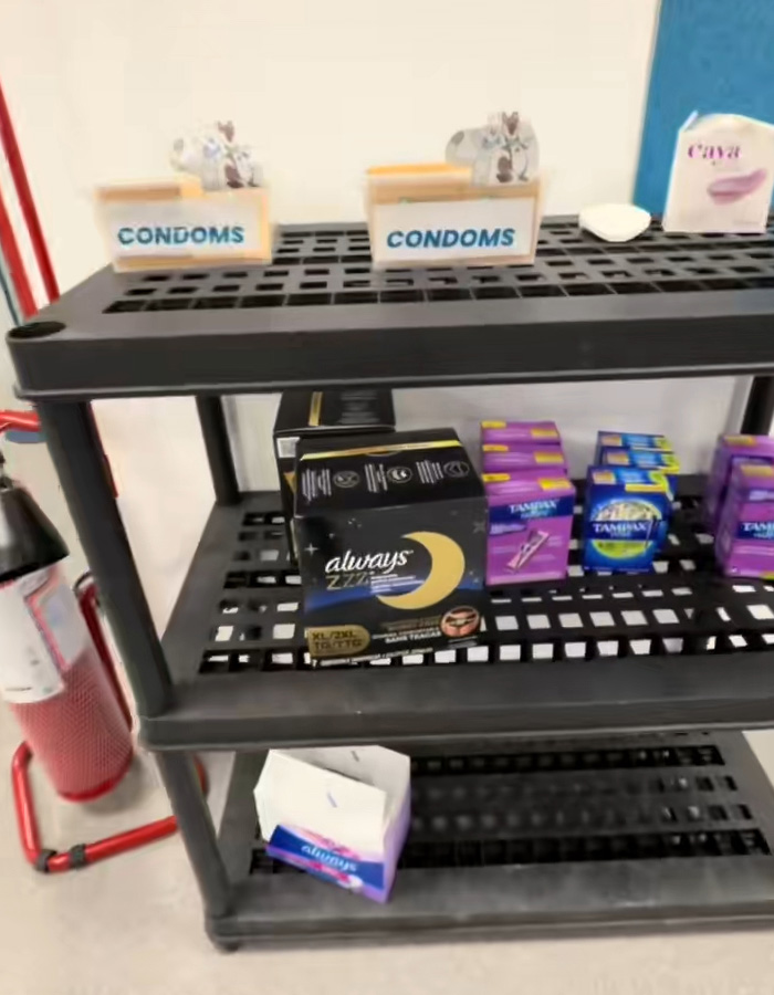 C****m boxes on a black shelf with menstrual products below, highlighting Olympic Village running out of rubbers quickly.