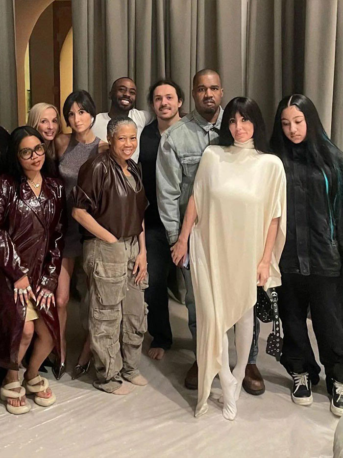 Grupo de pessoas posando em ambiente fechado, com Bianca Censori vestindo uma roupa estilosa com top de lingerie.