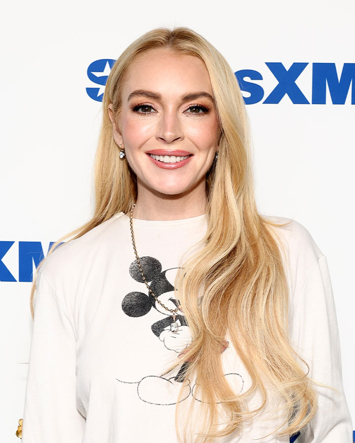Lindsay Lohan smiling at a media event, highlighting the dark side of growing up famous in a candid interview.
