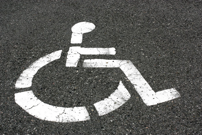 Handicapped parking spot symbol painted on asphalt, representing accessibility and challenges in parking drama situations.