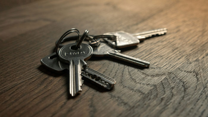 Set of metal spare keys lying on a wooden surface symbolizing a roommate&rsquo;s parents using a spare key to enter.