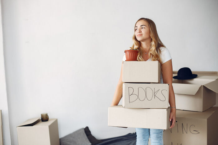 Young woman carrying moving boxes labeled books, symbolizing a brutal wake-up call to remove herself from a nasty situation immediately.