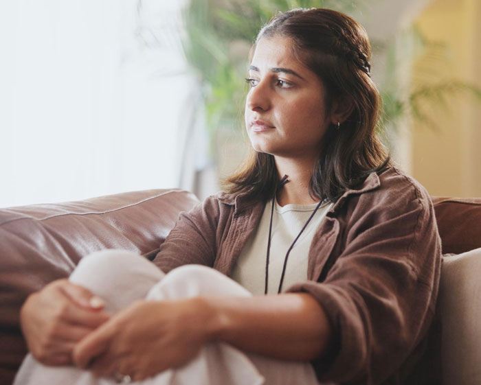 Thoughtful woman sitting on a couch, reflecting on issues related to birth mom claims and DNA access concerns.
