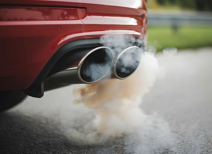 Car exhaust emitting smoke on a road, illustrating dangerous things that are often dismissed by people.