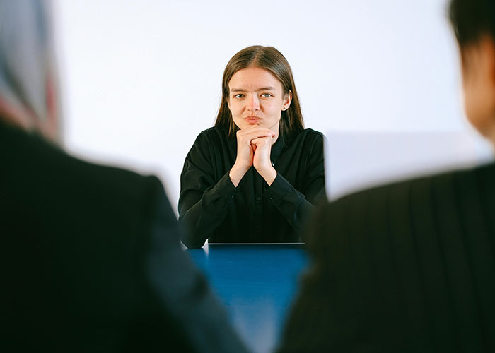 Young woman in black shirt sitting at a table with two blurred coworkers, showing signs of frustration and entitlement.