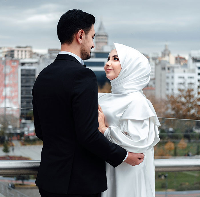 Woman and man in wedding attire embracing outdoors with cityscape background, symbolizing marriage and big secret reveal.