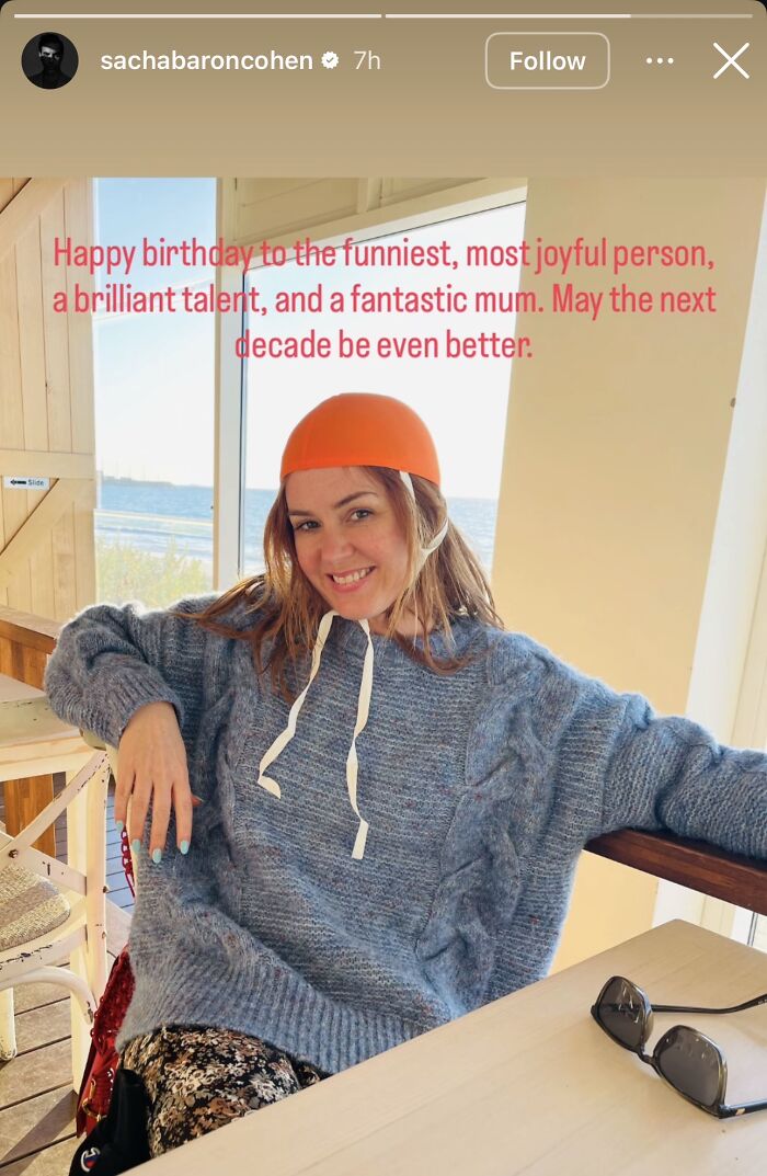 Isla Fisher smiling indoors wearing a knit sweater and orange cap in a rare message from Sacha Baron Cohen after divorce.