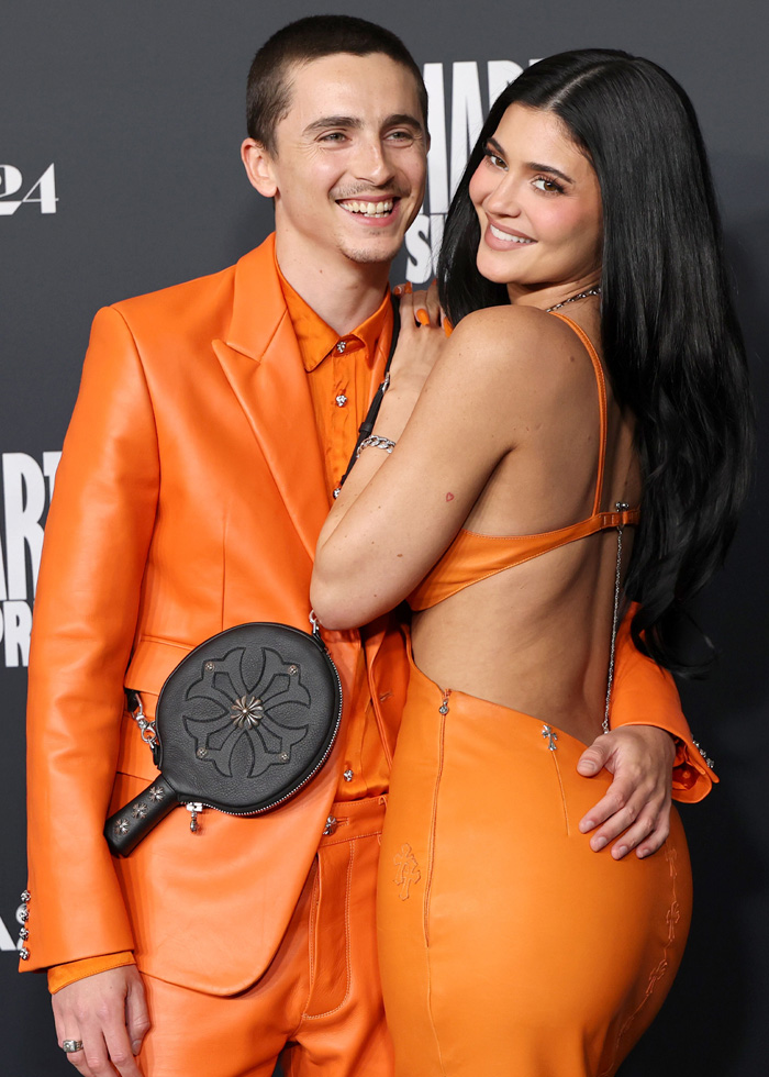 Timoth&eacute;e Chalamet and woman in matching orange outfits at event, sparking hotel appearance conspiracy theories.