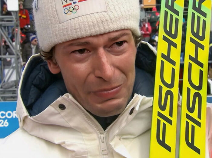 Olympian in winter gear holding skis, showing an emotional expression after live TV confession of cheating.