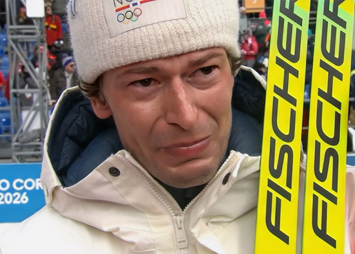 Olympic medalist wearing white jacket and beanie, holding skis, emotional after surprising cheating confession.