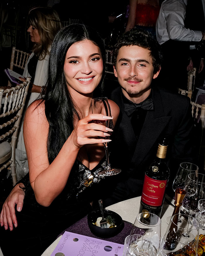 Kylie Jenner smiling with drink in hand, attending the 2026 BAFTAs, fans notice a major lip detail.