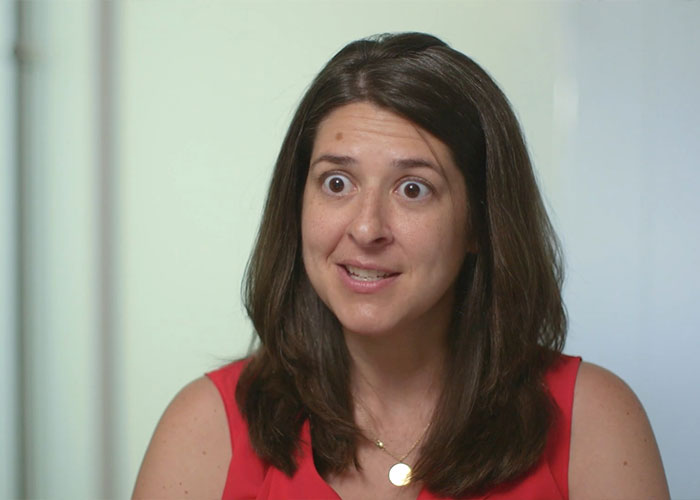 Woman teacher in a red top with shocked expression reacting to an abhorrent hot-mic moment causing student outrage