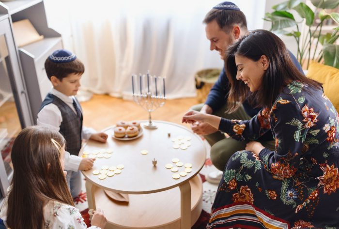 Family playing dreidel around a table with Hanukkah gelt and a menorah, celebrating the Google dreidel activity. Family playing dreidel around a table with Hanukkah gelt and a menorah, celebrating the Google dreidel activity.