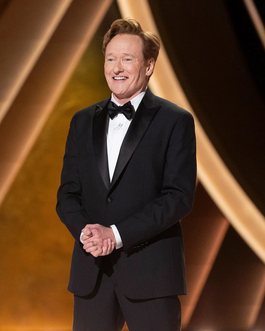 Conan O’Brien in a black tuxedo smiling on stage during a formal Oscars 2026 event with warm golden lighting in the background. Conan O’Brien in a black tuxedo smiling on stage during a formal Oscars 2026 event with warm golden lighting in the background.