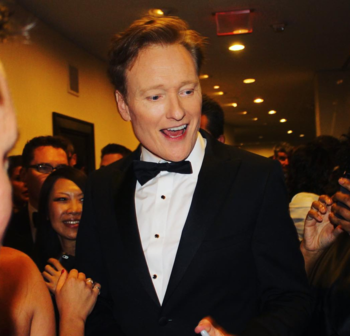 Conan O&rsquo;Brien in a black tuxedo smiling and interacting with a crowd at a formal Oscars event.
