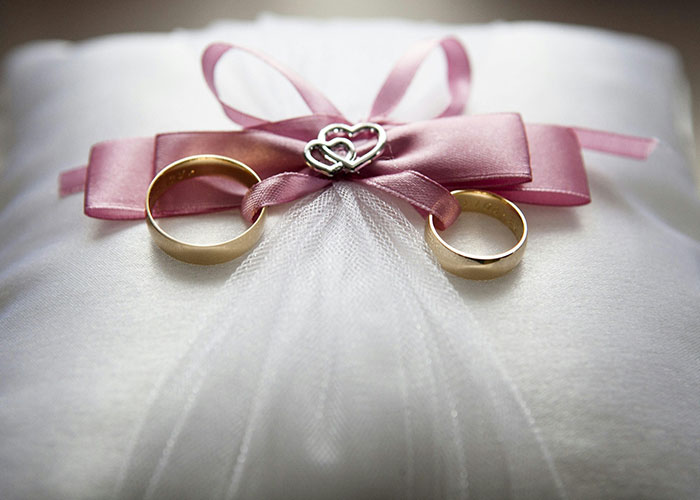 Wedding rings placed on a white pillow with a pink ribbon, representing tension between teen and stepmom on wedding day.