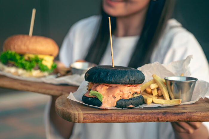 Person holding wooden trays with a black bun burger and fries symbolizing brutal wake-up calls to leave nasty situations fast.