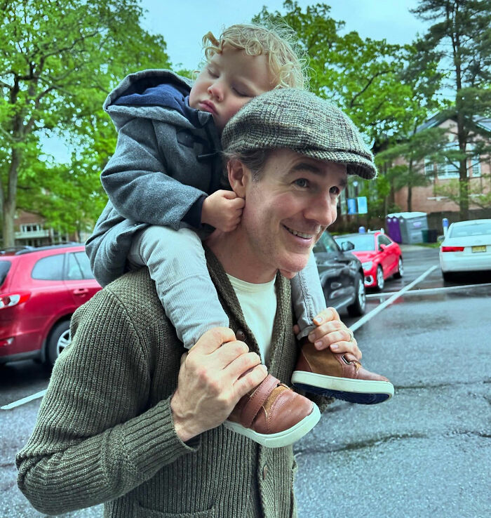 Man wearing a cap smiling with a sleeping child on his shoulders in a parking lot, symbolizing James Van Der Beek&rsquo;s final days.