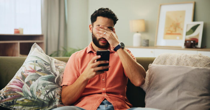 Man sitting on a couch looking frustrated while holding a phone, illustrating wildest dating experiences and reality doubts.