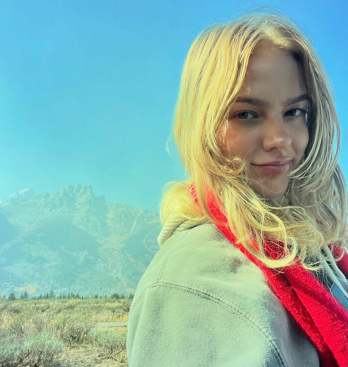 Young woman hiking New York's highest peak with her dog, surrounded by mountains and clear blue sky.