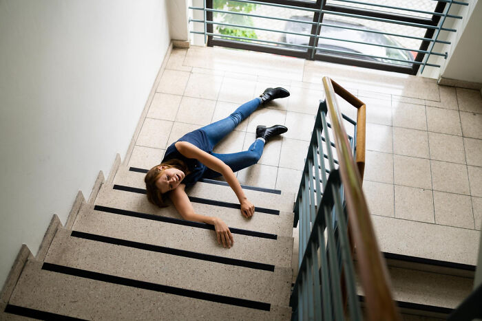 Woman lying on stairs injured, illustrating dangerous things often dismissed as minor risks in daily life situations.
