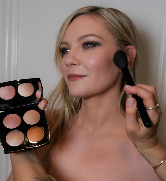 Kirsten Dunst applying makeup with a brush, highlighting her face before the 2026 BAFTA's fashion event.